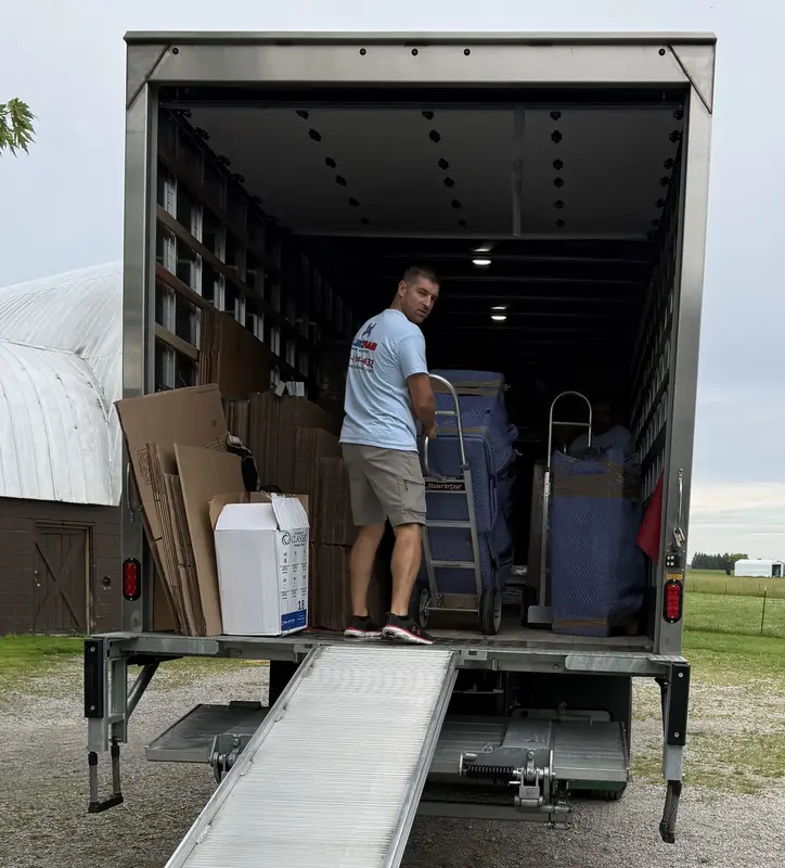 Blue Crab mover loading a hand truck of wrapped furniture into the moving truck.